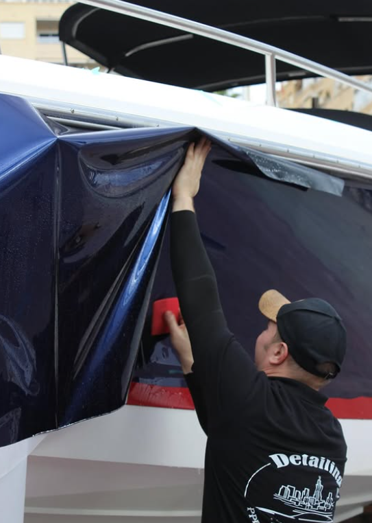 Instalación de lámina azul oscuro con espátula en el casco de un yate en Alicante